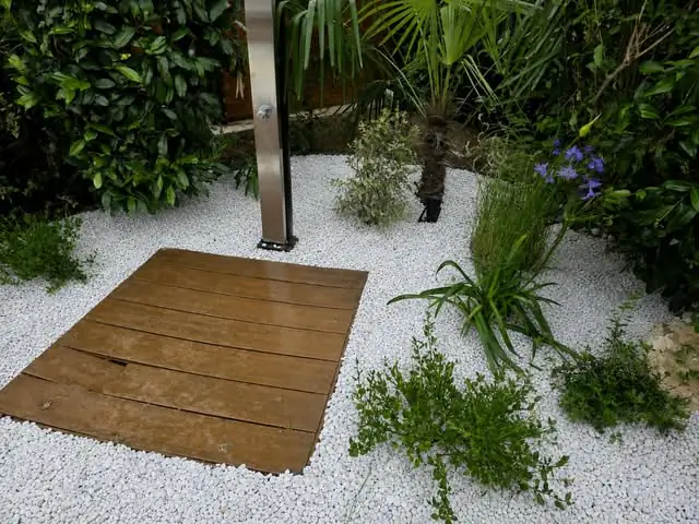 Aménagement paysager avec gravier blanc, plantes et passage en bois